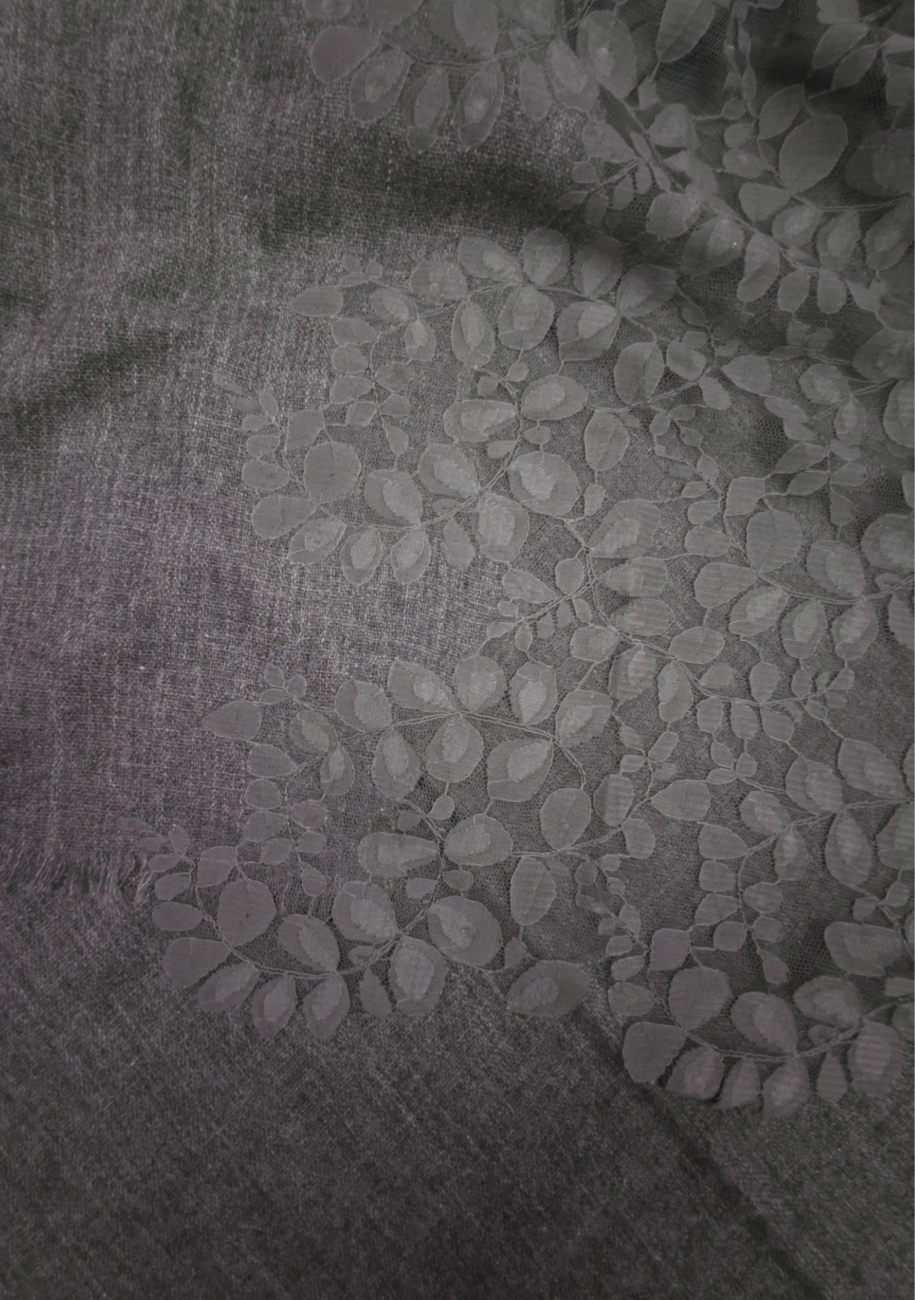 A close-up of a dark gray textured fabric with a lighter gray floral or leafy woven pattern across the surface.