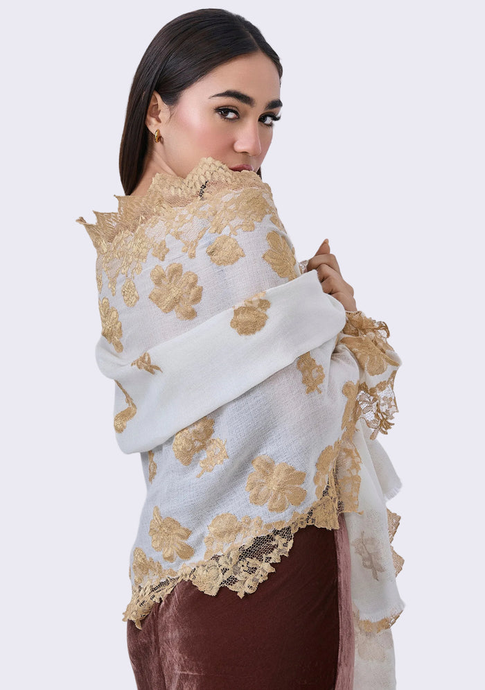 A woman showcasing an ivory cashmere scarf with gold lace borders wrapped around her neck.