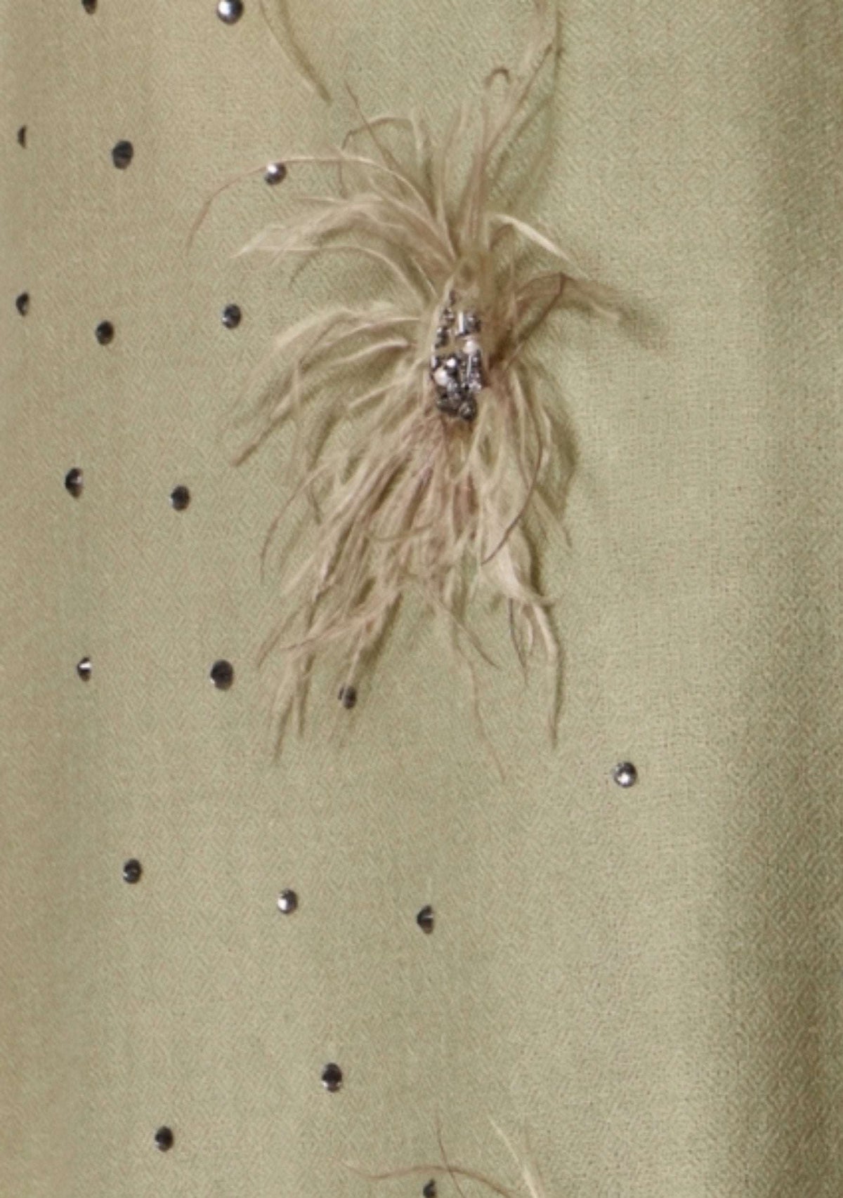 Close-up of a shawl surface decorated with scattered silver rhinestones and a central feather embellishment with a metallic embroidery and swarovski crystals