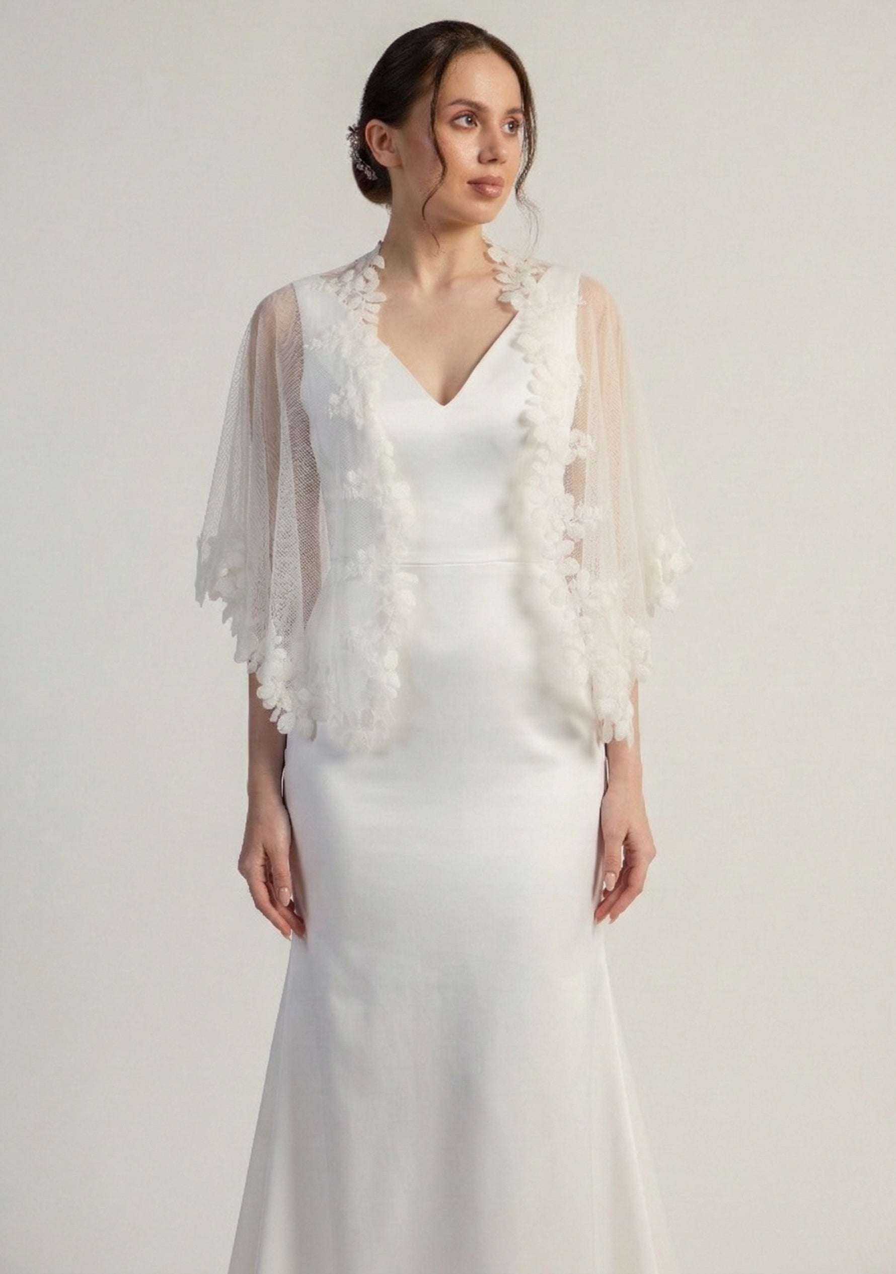 Woman wearing a white wedding dress with a floral shrug against a plain background
