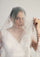 Woman wearing a white wedding dress with a veil against a plain background