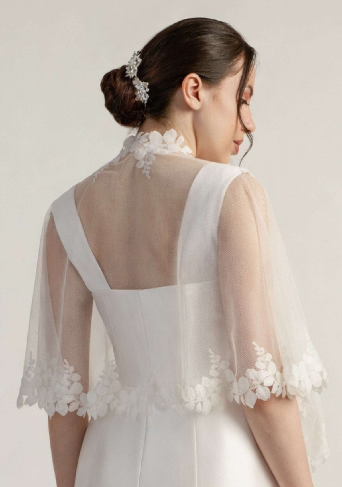 Woman wearing a white lace bridal shrug against a plain background