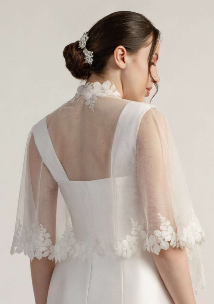 Woman wearing a white lace bridal shrug against a plain background