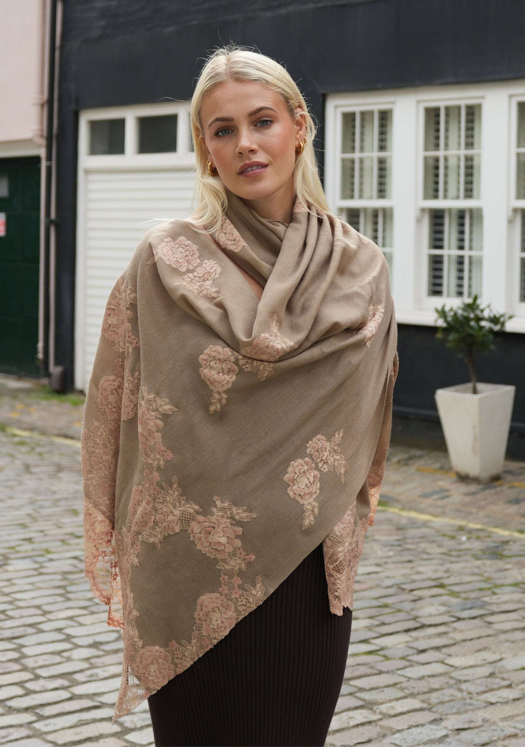 A woman wearing a natural color cashmere scarf with dual shade copper Chantilly lace, draped around her neck.