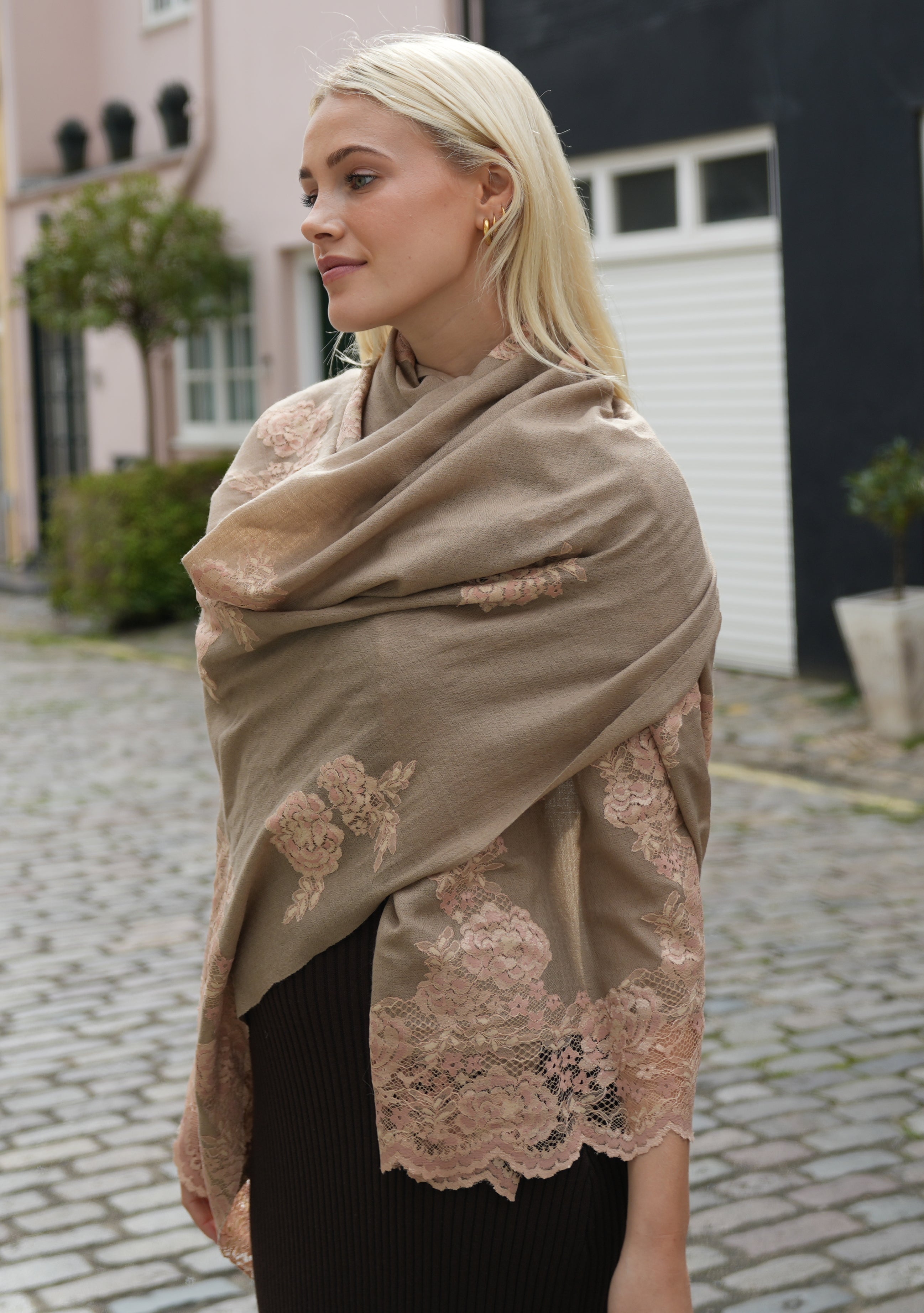 A woman wearing a natural color cashmere scarf with dual shade copper Chantilly lace, draped around her neck.