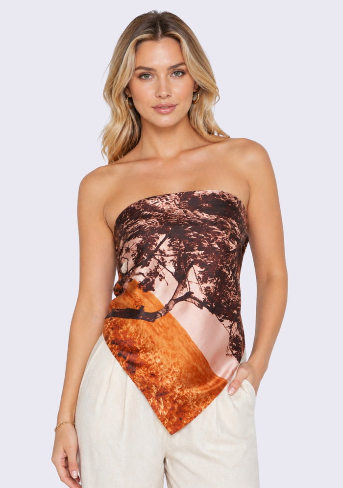 Santa Cruz Print Silk Square Scarf by Maneesha Ruia styled as a chic strapless silk top, featuring a coastal-inspired print in warm coral, rust orange, blush pink, and deep brown, paired with ivory trousers for a luxury resort look.