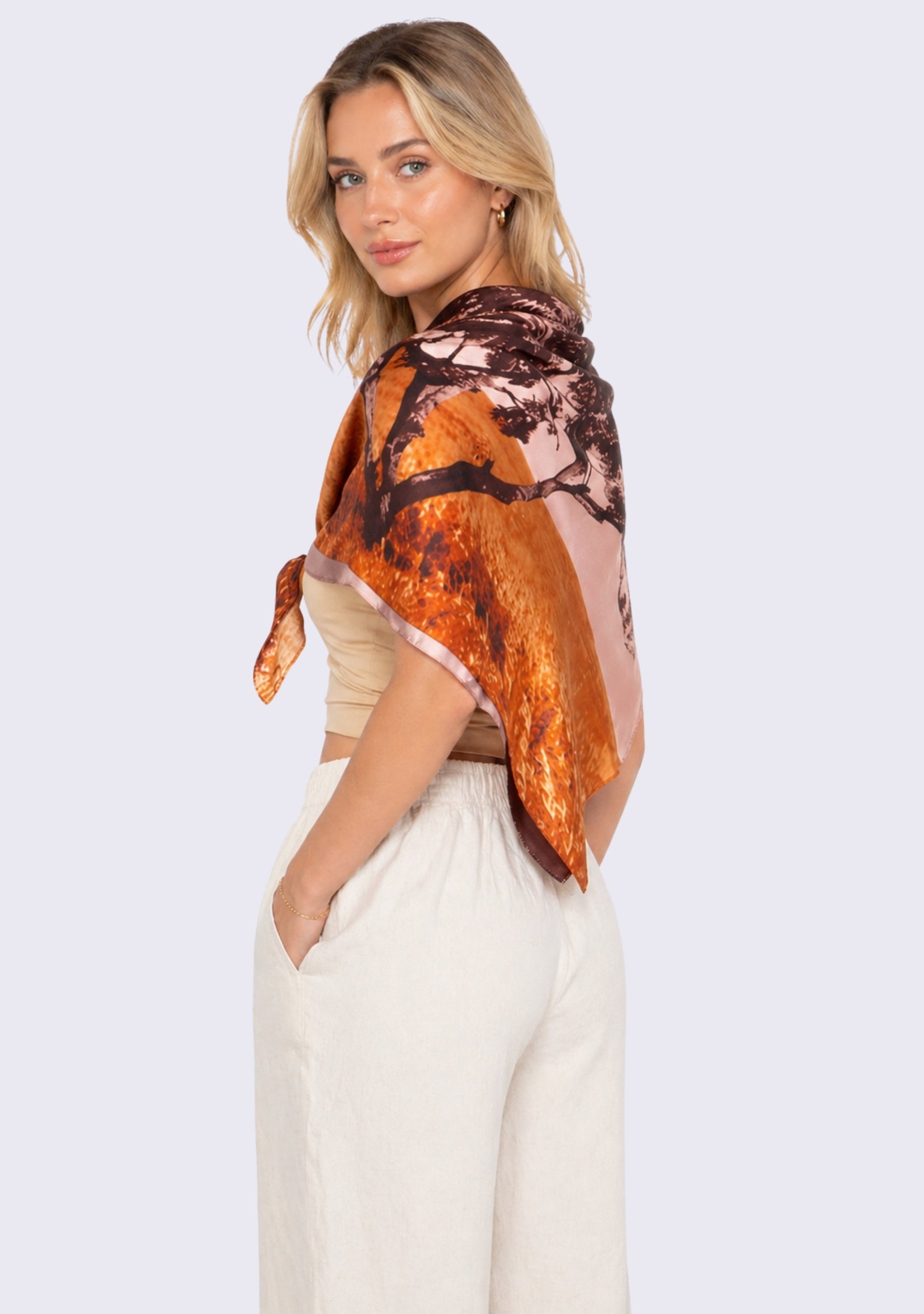 Santa Cruz Print Silk Square Scarf by Maneesha Ruia draped over the shoulders, showcasing a coastal-inspired print in warm coral, rust orange, blush pink, and deep brown on luxurious 100% silk, styled with an elegant neutral outfit.