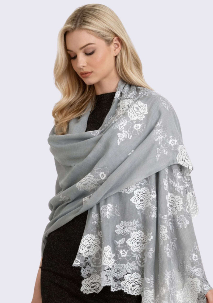 Luxury silver gray cashmere scarf with delicate light blue Chantilly floral lace, elegantly draped on a female model in a sleeveless dress. Soft, lightweight designer cashmere wrap with intricate handcrafted lace, perfect for weddings, evening wear, formal occasions, and timeless luxury styling.