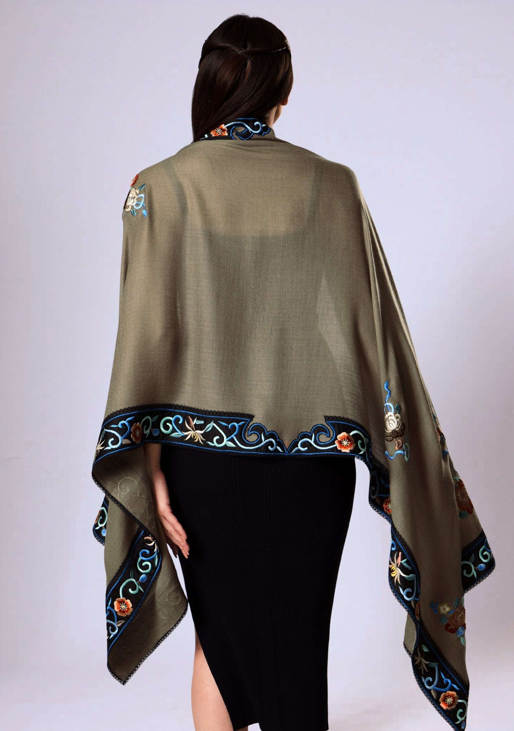 a woman wearing a taupe cashmere multi colored embroidered scarf over a black outfit on a white background