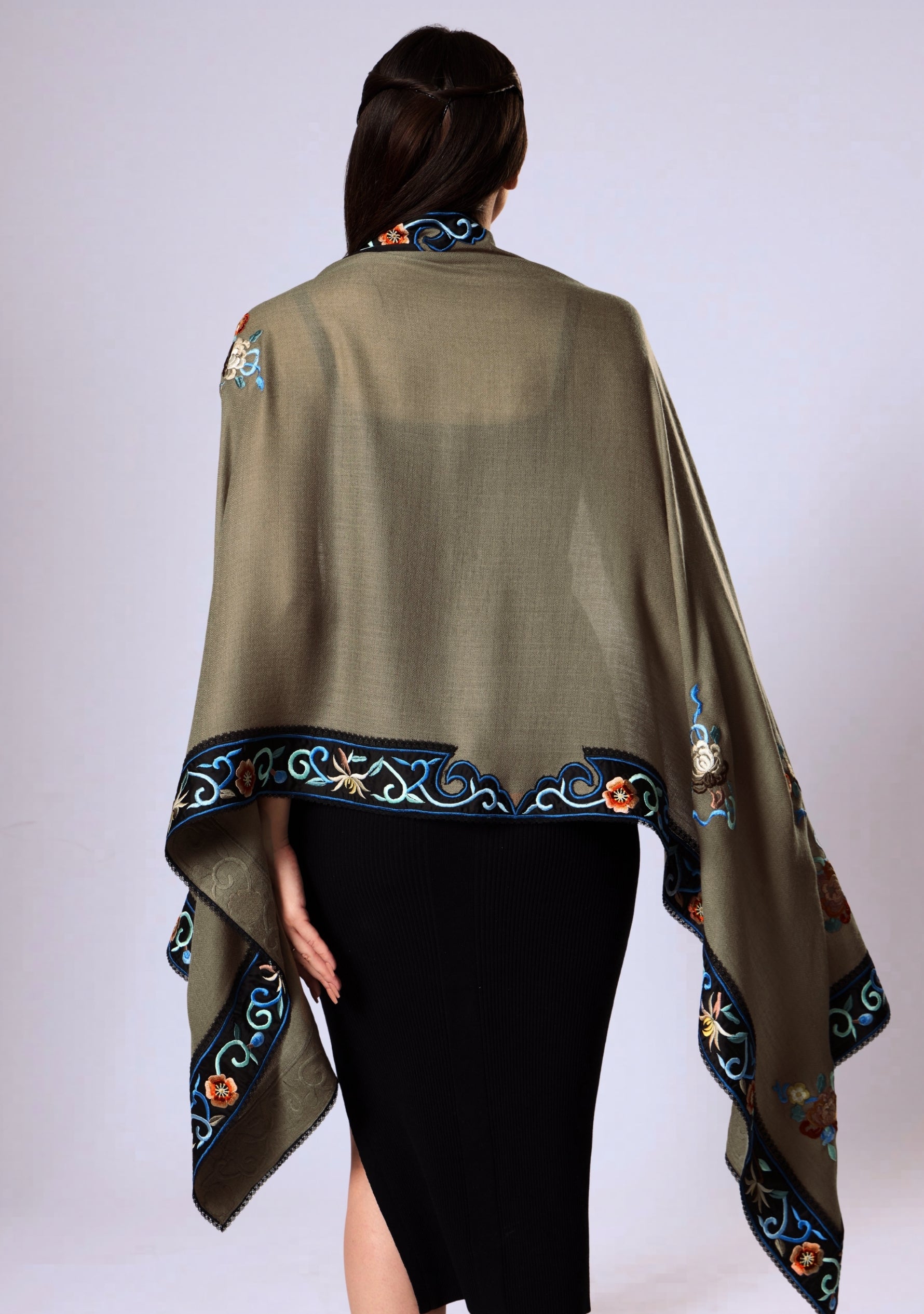 a woman wearing a taupe cashmere multi colored embroidered scarf over a black outfit on a white background