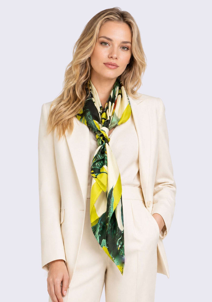 Toucan Print Silk Square Scarf by Maneesha Ruia elegantly tied around the neck, featuring vibrant tropical foliage, exotic toucan motifs, lush emerald green leaves, lime green accents, and ivory tones on luxurious 100% silk.