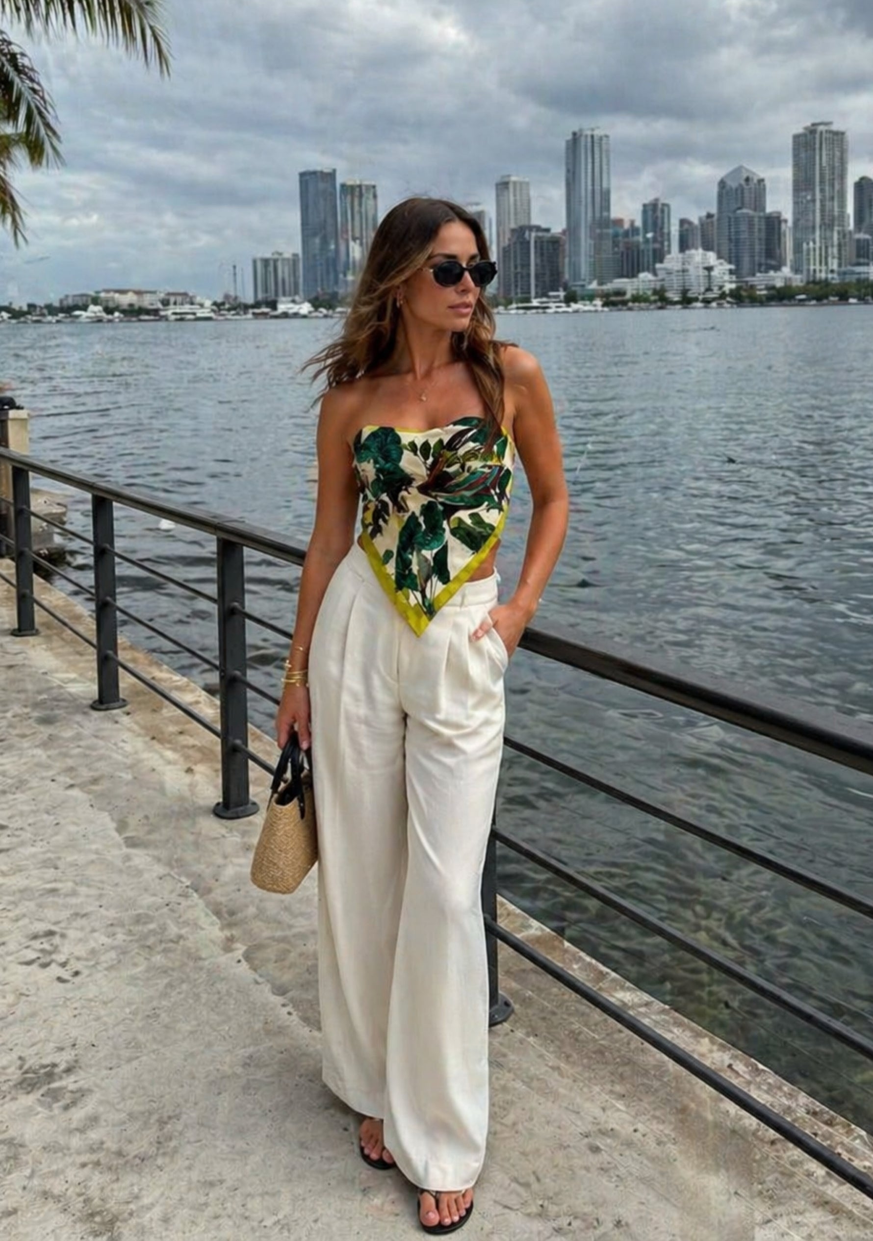 Toucan Print Silk Square Scarf by Maneesha Ruia styled as a chic strapless silk top, featuring a vibrant tropical print with lush green foliage, exotic toucan motifs, and lime green accents, paired with white wide-leg trousers for a luxury resort look.