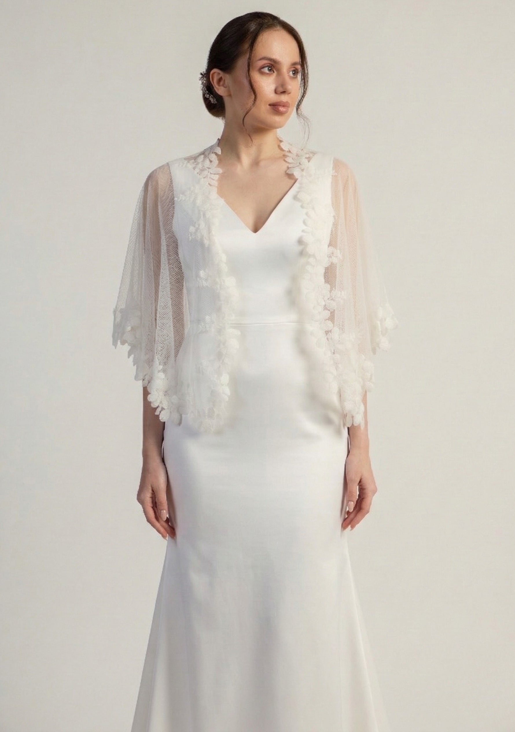 Woman wearing a white wedding dress with a floral shrug against a plain background
